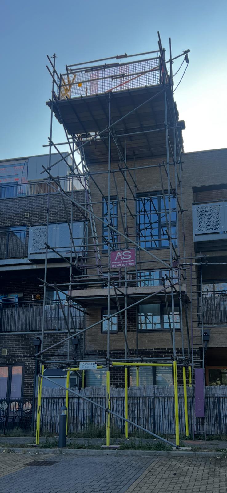 Armstrong Scaffolding hoist and lifting tower with elevated material loading bay, brick guards and edge protection erected to a multi-storey residential apartment block in London