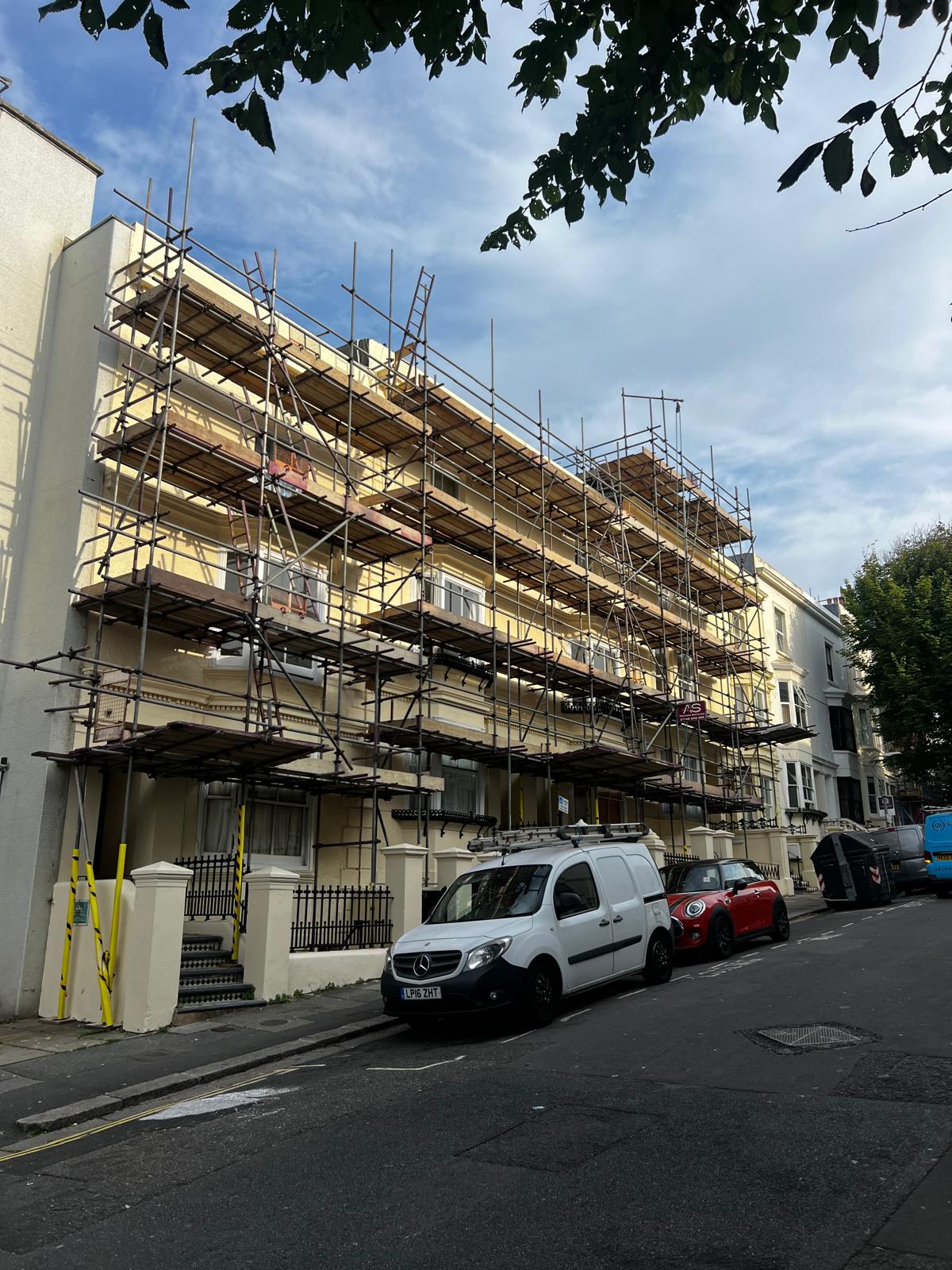 Armstrong Scaffolding full-height safe access scaffold with timber boarded working platforms and edge protection erected to a cream Regency terrace in Brighton for exterior maintenance and refurbishment works