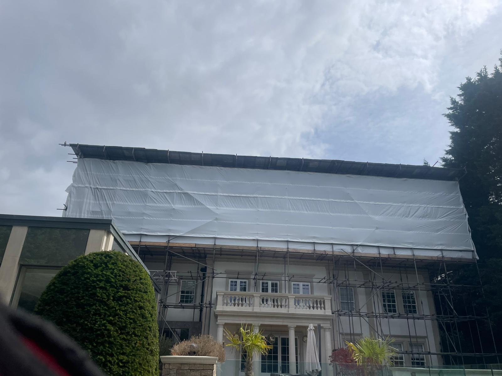 Close-up front elevation of an Armstrong Scaffolding temporary roof with white shrink-wrap sheeting tightly tensioned over the scaffold framework, providing complete waterproof weather protection for a residential property during roof works