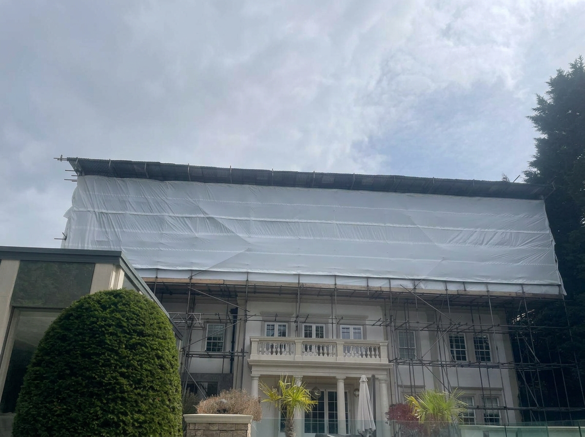 Armstrong Scaffolding temporary roof with shrink-wrap encapsulation over a residential property at Woodlands, Keston Park, Orpington, with full perimeter scaffold, beamed-over car lift and 300kg hoist tower for roof works access