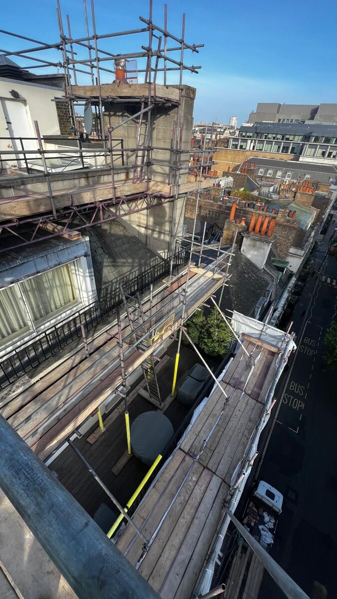 Armstrong Scaffolding chimney stack scaffold seen from roof level, with boarded lifts wrapping the building and the Mayfair street far below