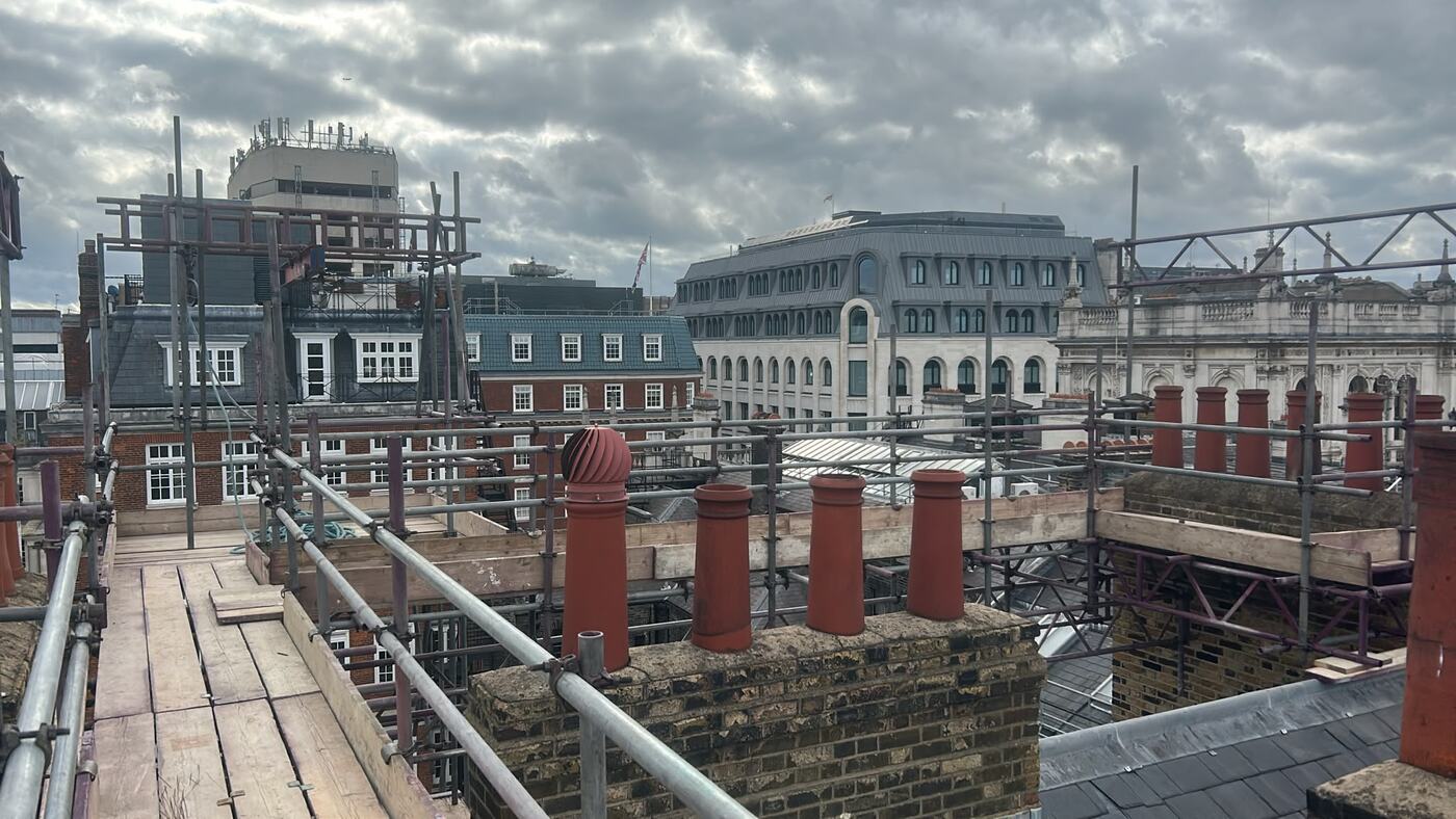 Chimney stack scaffolding in Piccadilly London, boarded walkway and guardrails at roof level between brick stacks with red clay pots
