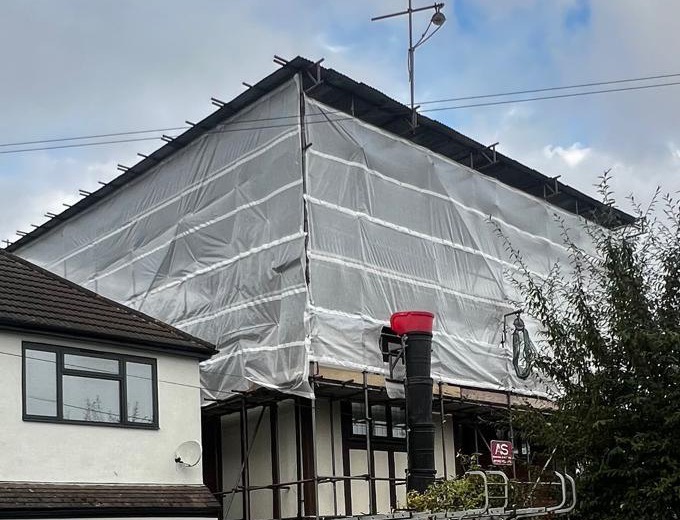 Red chute hopper at scaffold level with the debris chute running to ground, below a pitched temporary roof oversailing the house in Hayes, Bromley