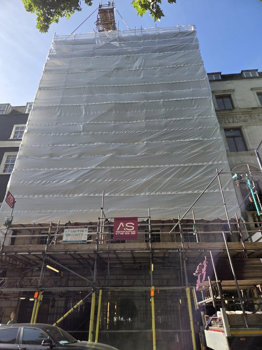 Fully encapsulated Armstrong Scaffolding structure on Berkeley Square with the boarded pedestrian gantry and company banner at street level
