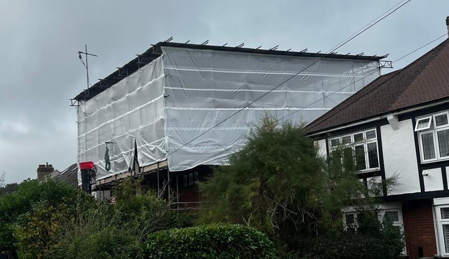 Encapsulated scaffold and pitched temporary roof seen from the side in Hayes, Bromley, with the neighbouring house alongside