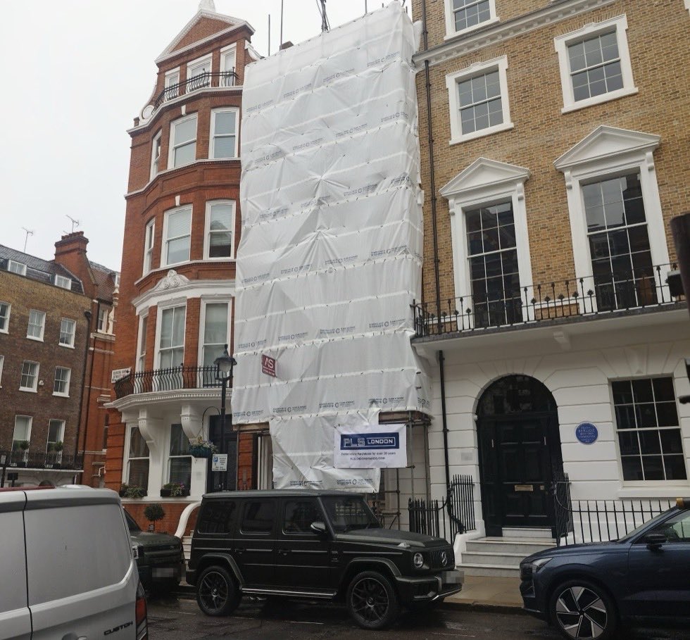 Full height scaffold clad in flame retardant sheeting on a townhouse in Queen Anne Street, Marylebone, between two neighbouring period buildings