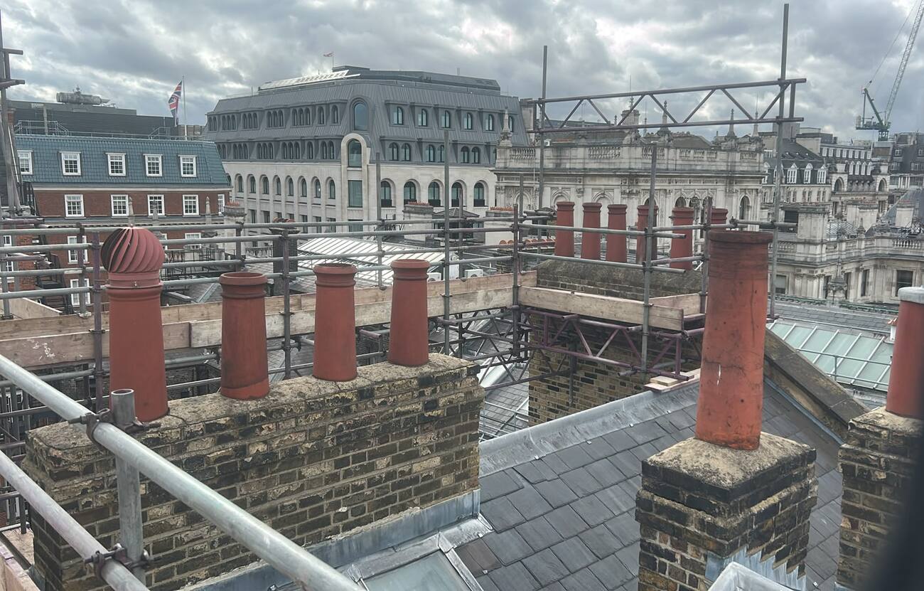 Roof level walkway scaffold boarded above slate between chimney stacks on a central London building