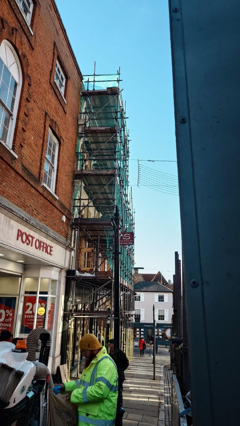 Boarded pedestrian route running beneath the Armstrong Scaffolding façade scaffold past the shopfronts on Guildford High Street